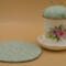 This shows the pincushion bobbin holder next to the trivet. The trivet is about 5.5 inches wide. Flower is on saucer to left of cup.